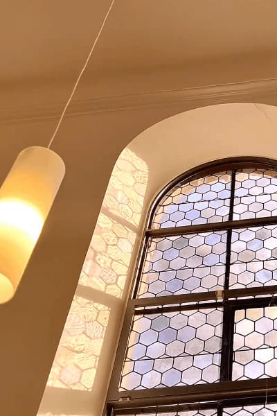 Bogenfenster mit Bleiverglasung und eine Lampe im Kirchraum